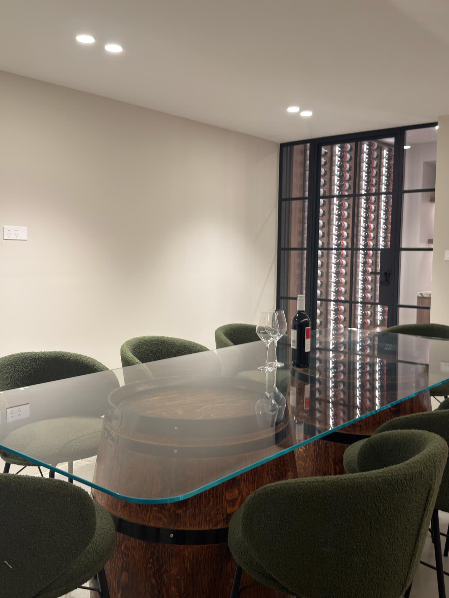 Glass-topped dining table beside a lit wine cellar
